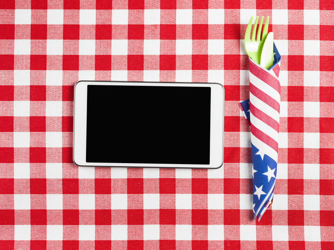 A smart phone on a picnic table with plastic cutlery for July 4th